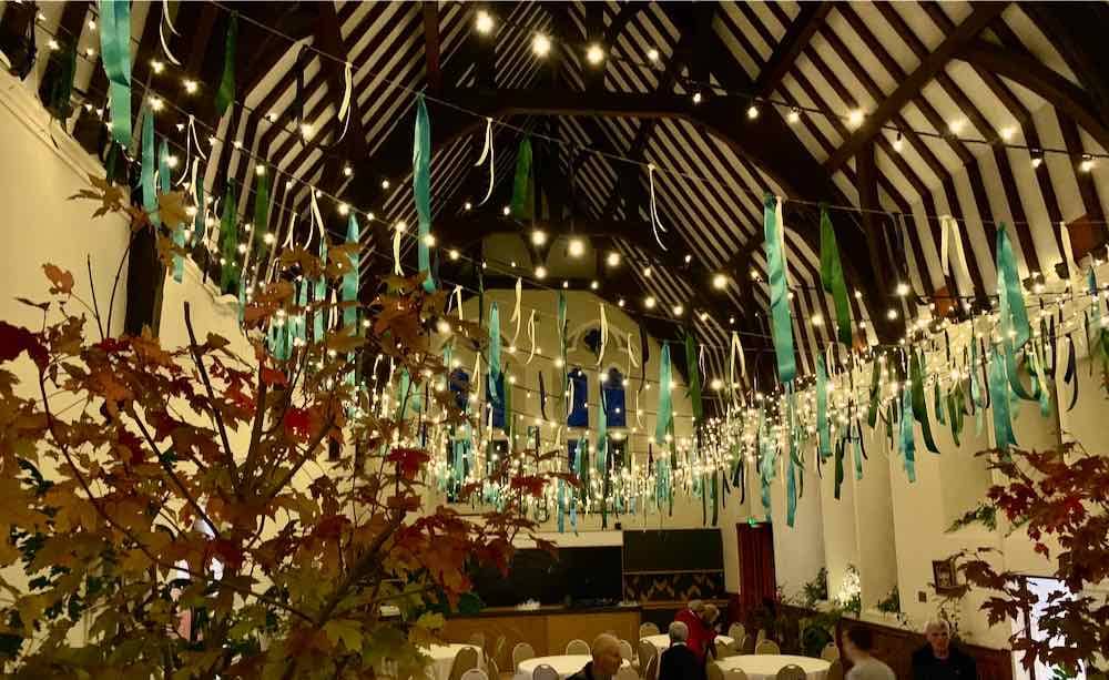 Westbury On Trym Village Hall Charm: Wooden beams grace the interior, casting a rustic allure. Fairy lights adorned with delicate silk tassels hang from above, infusing the space with a whimsical and enchanting atmosphere.