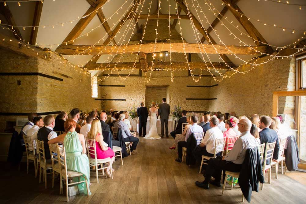 Bath's Wick Farm Elegance: At Wick Farm Wedding Venue in Bath, a stylish fairy-light canopy sets the stage for enchantment. Underneath, a bride and groom stand surrounded by friends on either side, creating a picture-perfect moment of joy and celebration in the heart of this beautiful venue.
