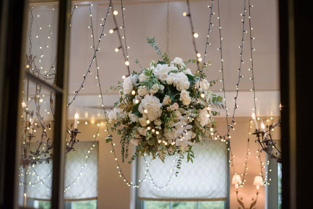 A flower ball suspended from the ceiling of a ding room with fairy-lights either side in the daytime
