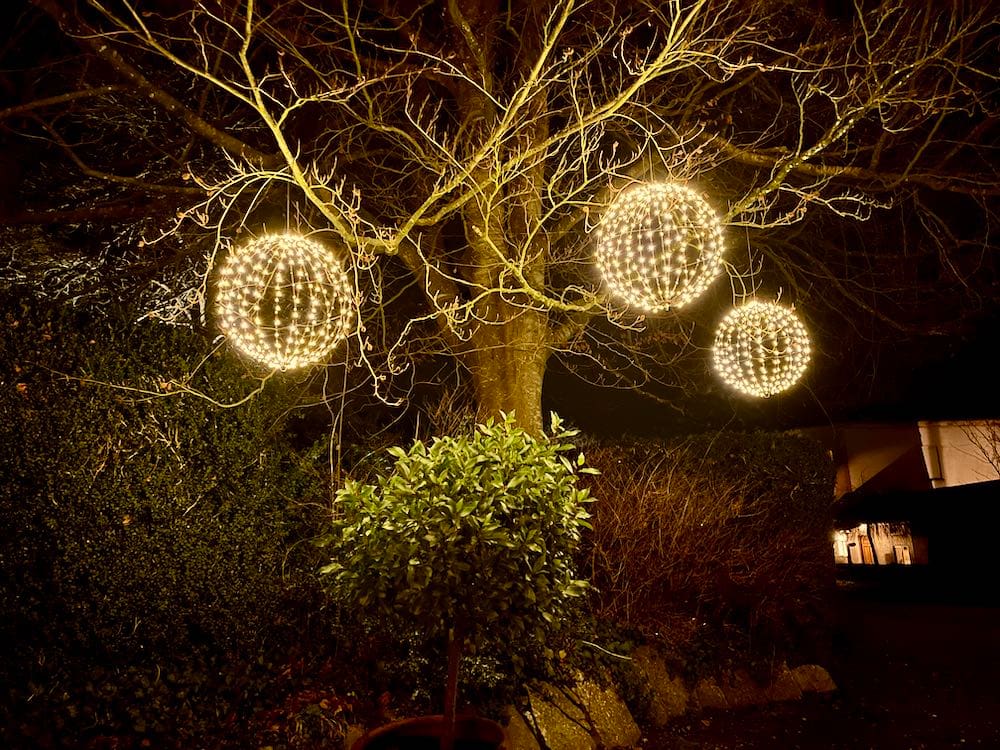 Mystical Nighttime Silhouette: Against the dark night sky, a bare tree trunk takes center stage, adorned with three large LED spheres hanging from its branches. The spheres cast a soft and otherworldly glow, creating a mystical and enchanting atmosphere in the quiet of the night.