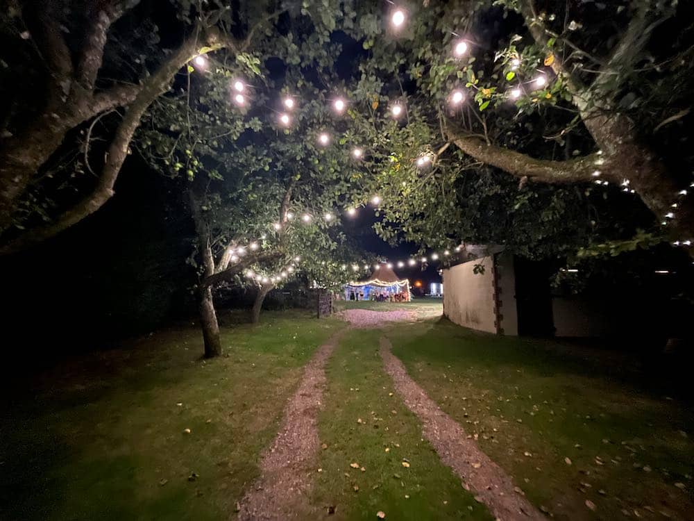 Nighttime Path of Radiance: Under the night sky, a grass track adorned with festoon lighting extends like a luminous pathway, rigged in trees and leading the way to a wedding marquee. The warm glow from the lights creates a magical journey, guiding guests to the heart of the celebration in the enchanting darkness.