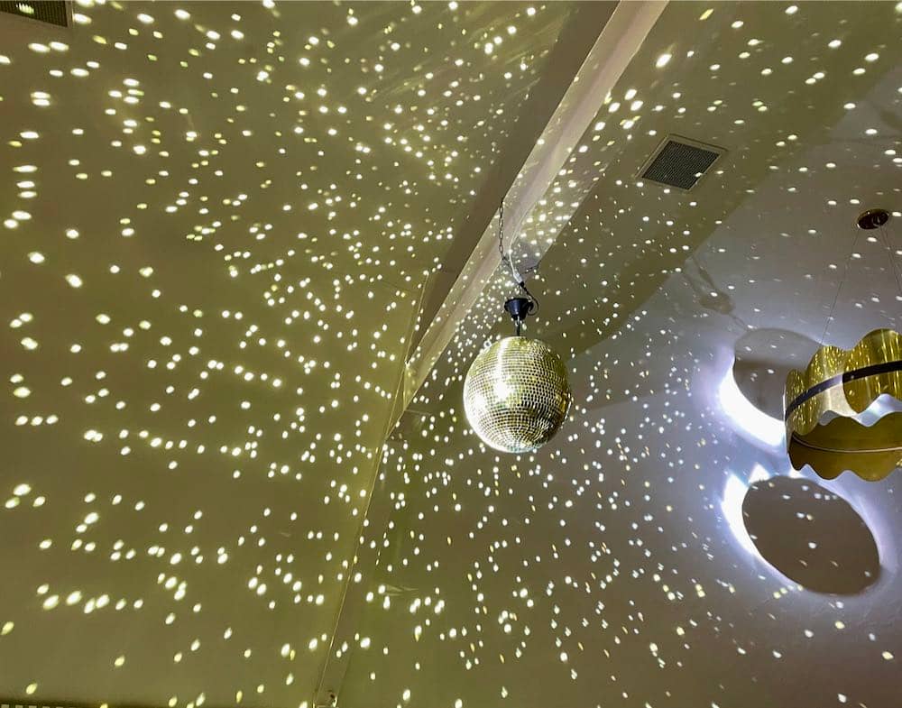 Centered and captivating, a mirror ball captures the spotlight, casting reflections of gold lighting on the ceiling above. The play of lights creates a dazzling and glamorous ambiance, adding a touch of magic to the surroundings.