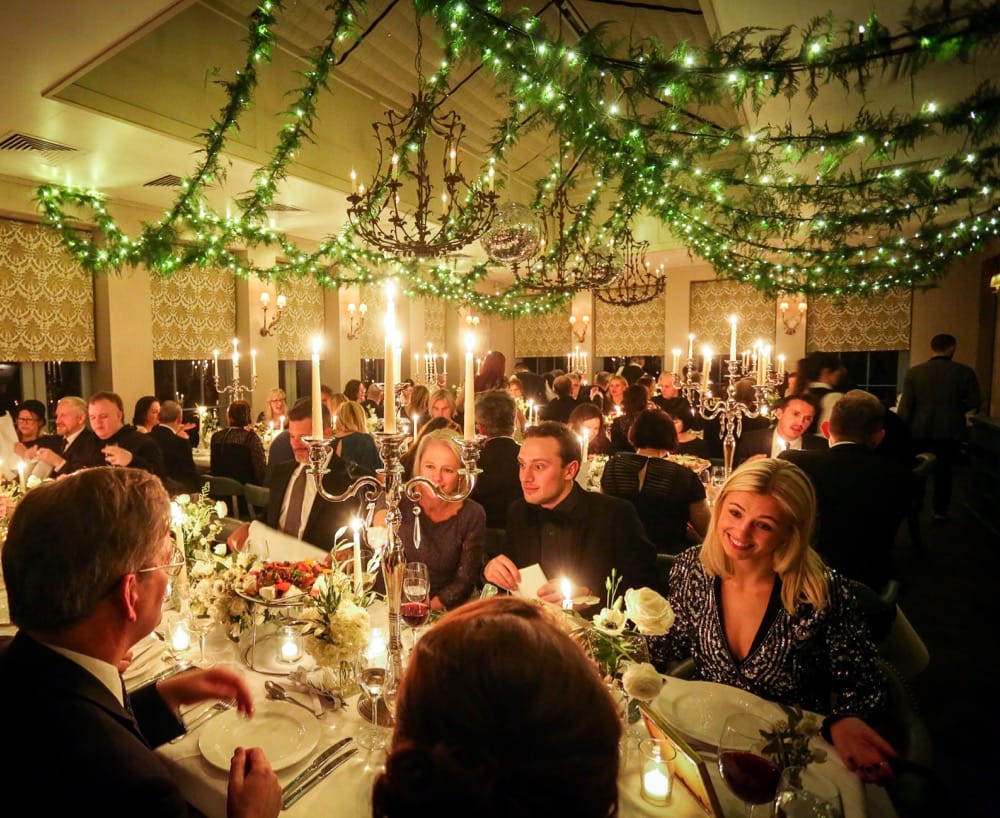 Enchanting Orangery Night: The Orangery at Babington House comes alive at night with a magical wedding breakfast. Numerous guests are seated under a canopy of fairy lights delicately wrapped in asparagus, casting a warm and intimate glow. Candleabras and candles add to the romantic atmosphere, creating a captivating setting for the celebration.