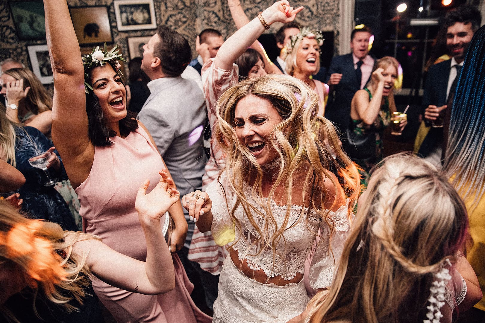 Celebratory Bliss: At the heart of the dance floor, the bride stands with her hair in the air, surrounded by friends, all joyously dancing together. The scene radiates with celebratory bliss, capturing the vibrant energy of the wedding festivities