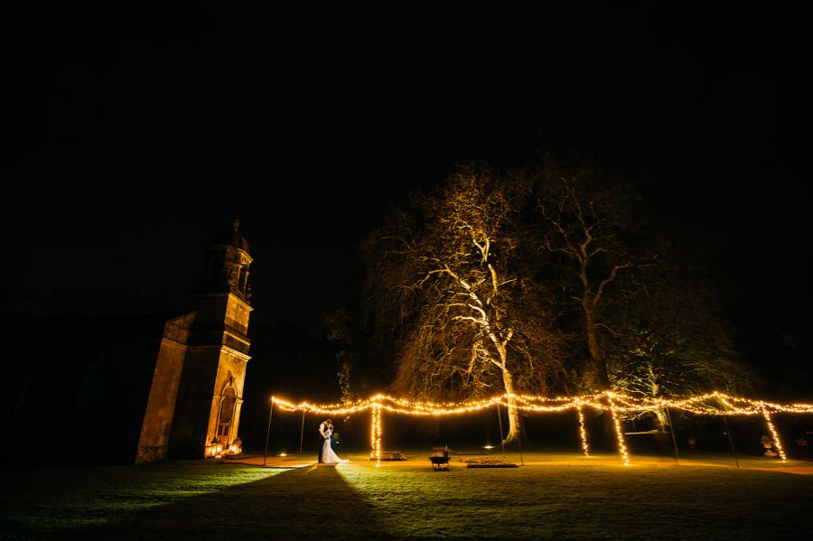 Nighttime Romance at St. Margaret's, Babington: A picturesque scene unfolds in the night at St. Margaret's, Babington, Somerset. A wedding lighting tunnel guides the way to the church, where a bride and groom embrace underneath, surrounded by the enchanting glow, creating a moment of timeless romance.